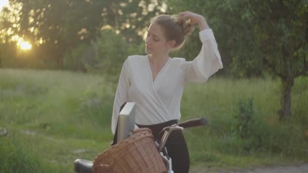 Retrato de mujer elegante y confiada desatando el cabello en el parque de verano por la noche. plano medio de hermosa delgada dama de negocios caucásica descansando al aire libre al atardecer . — Vídeos de Stock