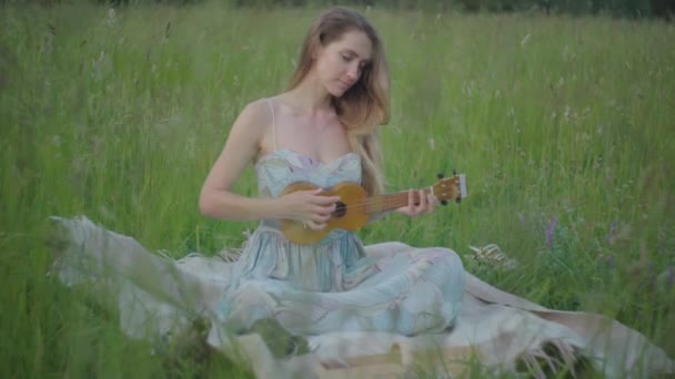 Affascinante musicista donna che suona ukulele sul prato verde. Ritratto di giovane donna caucasica positiva che si gode la giornata nel soleggiato parco estivo. Tempo libero, stile di vita, hobby, felicità. — Video Stock