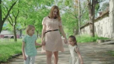 Neşeli kız ve oğlanın el ele tutuşup Sunny Park 'taki ara sokakta yürüyen çekici genç annenin ön görüntüsü. Yazı çocuklarla geçiren Kafkasyalı sarışın kadının portresi.