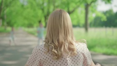 Sarışın, beyaz bir kadının yaz parkında sokakta oturduğunu ve çocukların ona doğru koştuğunu gördüm. Neşeli kız annesine sarılıyor, oğlu önünden geçiyor. Aile açık havada güneşli bir gün geçiriyor..