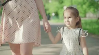 Güneşli parkta annemle gezen esmer, güzel bir kızın portresi. Annesinin elini tutan ve dışarıda yaz gününün tadını çıkaran sevimli beyaz kız çocuğu. Çocukluk, eğlence..