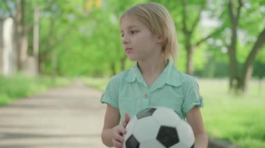 Futbol topuyla etrafta koşuşturan neşeli kız kardeşine bağıran sarışın çocuğun orta pozu. Kardeşinin güneşli yaz parkında kardeşiyle tartışması tatmin edici değil. Çatışma, aile ilişkisi.