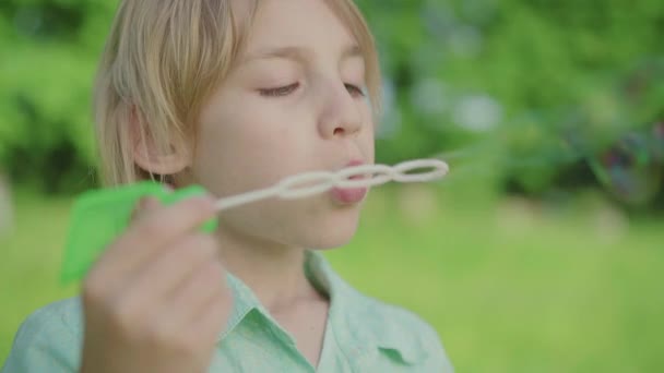 Gros plan sur le visage de charmant garçon blond caucasien soufflant des bulles de savon à l'extérieur. Portrait de mignon petit enfant qui s'amuse dans un parc vert ensoleillé d'été. Loisirs, enfance, joie, mode de vie.