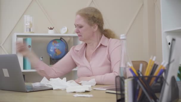 Mad Caucasian woman crying, putting on headphones and start dancing to music in earphones. Portrait of emotionally unstable person sitting at the table indoors. Personality disorder, mental illness. — Stock Video