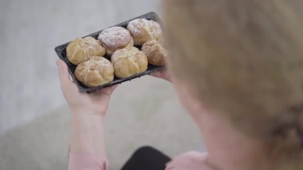 Vista superior de saborosos pães doces em mãos femininas seniores. Mulher caucasiana ruiva irreconhecível que cheira deliciosa padaria fresca. Alimentos não saudáveis, dieta, calorias . — Vídeo de Stock