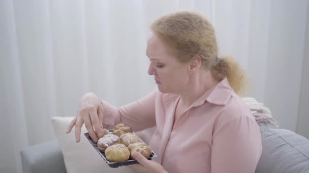 Στεναχωρημένη παχουλή γυναίκα που μασάει γλυκά ψωμάκια και κλαίει. Πλευρική άποψη του άγχους Καυκάσιος ηλικιωμένη κυρία έχει κατάθλιψη. Θλίψη, πρόχειρο φαγητό, άγχος. — Αρχείο Βίντεο
