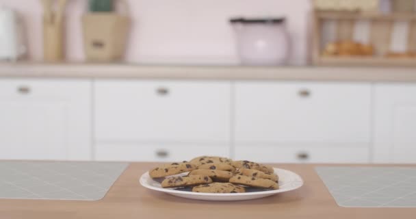 Leuke jongen die uit de tafel gluurt, rondkijkt en zoet lekker koekje neemt. Portret van een blanke jongen verstopt met een koekje in de keuken. — Stockvideo
