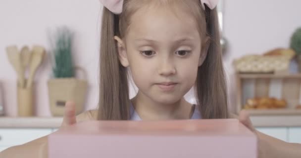 Großaufnahme des Gesichtes eines erstaunten kaukasischen Mädchens, das glühendes Geschenk öffnet und nach innen blickt. Porträt von charmanten brünetten Kind mit Pferdeschwanz begeistert mit Geschenk. — Stockvideo