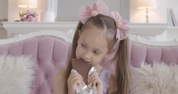 Πορτρέτο του γοητευτικού κοριτσιού που τρώει σοκολάτα. Μπρουνέτ Καυκάσιος, δαγκώνει γλυκό επιδόρπιο και μασάει. Παιδί απολαμβάνει ανθυγιεινά τρόφιμα στο σπίτι. — Αρχείο Βίντεο