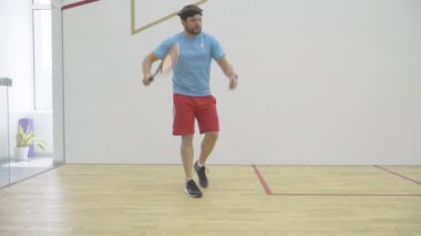 Spor salonunda beyaz tenli orta yaşlı sporcu eğitiminde geniş açı. Esmer, sakallı, atletik bir adamın evde egzersiz yaparken portresi. Kabak raketi ve top sporu oynayan kendine güvenen adam..
