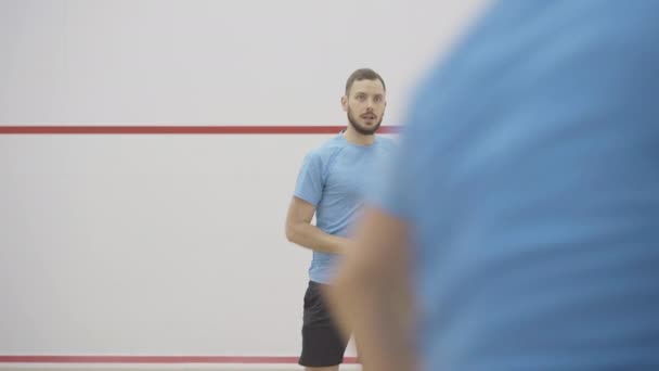 Spor salonunda tanınmayan bir sporcunun antrenmanını kontrol eden yakışıklı bir antrenörün portresi. Esmer, beyaz bir adam top servis ediyor ve önünde squash oynayan bulanık bir adam gibi konuşuyor.. — Stok video