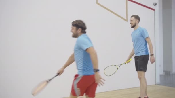Spor salonunda squash oynayan iki iyi konsantre sporcu. Beyaz adamların kapalı alanda antrenman yaptığı geniş açı. Spor kulübünde gülümseyen sakallı adamlar spor yapıyor.. — Stok video