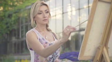 Açık hava manzarası çizen kahverengi gözlü kendine güvenen sarışın kadının portresi. Güneşli yaz gününde hobisinin tadını çıkaran güzel beyaz bir sanatçı. Parkta resim çizen ilham verici ressam.