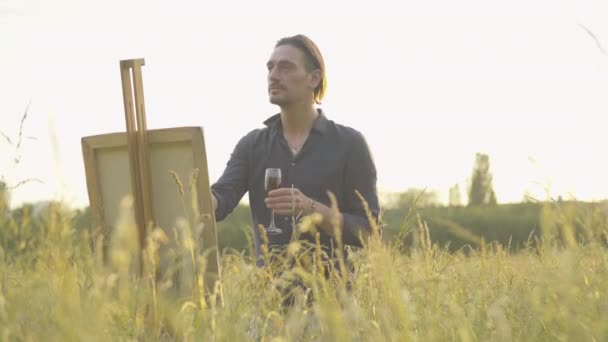 Kreativ man ritar bild vid solnedgången och dricker rött vin ur glas. Porträtt av självsäker koncentrerad kaukasisk konstnär målning landskap från naturen utomhus. Kreativitet, livsstil. — Stockvideo