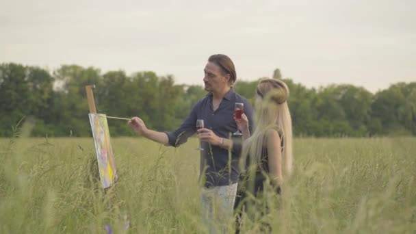 Zijaanzicht van zelfverzekerde schilder tekening beeld en klinkende wijnglazen met vrouw of vriendin. Knappe brunette Kaukasische man genieten hobby samen met partner bij zonsondergang buiten. — Stockvideo