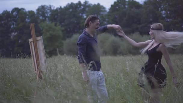 Gelukkige liefdevolle man en vrouw dansen op de zomerweide in de schemering. Portret van een glimlachend, vrolijk blank echtpaar dat samen in het weekend geniet. Liefde concept. — Stockvideo