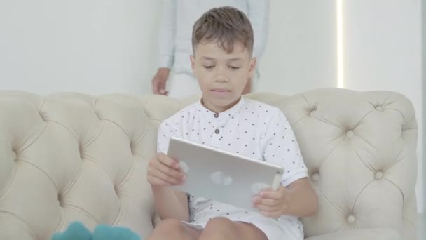一个在平板电脑上玩网络游戏的快乐的非洲裔美国男孩的肖像，他是一个难以辨认的母亲，走过来训斥他。严格的家长拿走装置。游戏成瘾概念、教育. — 图库视频影像