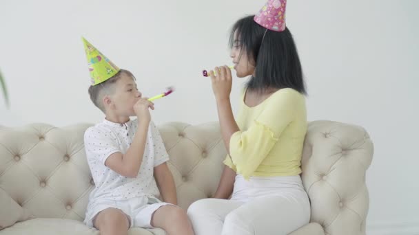 Retrato de mãe afro-americana feliz e filho soprando assobios de festa em casa. Mulher alegre e menino comemorando aniversário juntos dentro de casa. Felicidade e celebração conceito . — Vídeo de Stock