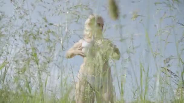 Femme blonde sexy dodue debout dans l'herbe verte à l'arrière-plan du ciel clair d'été et poitrine touchante. Portrait de dame en surpoids confiant posant à l'extérieur le jour ensoleillé. Corps positif. — Video