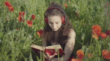 Kulaklıklı, açık havada kitap okuyan genç bir kadının portresi. Güzel, beyaz tenli esmer kadın çiçek çayırında oturmuş afyon tarlasında edebiyat ve müziğin tadını çıkarıyor. Hobi.