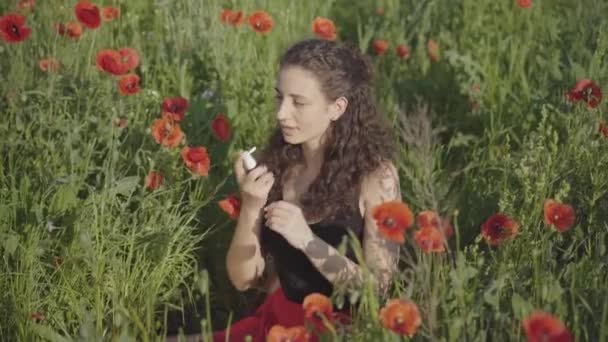 Giovane donna allergica caucasica spruzzando spray allergia seduto sul campo di fiori. Ritratto di bella signora caucasica magra che cura la malattia con farmaci sul prato soleggiato con papaveri rossi. — Video Stock