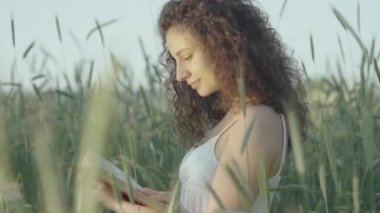 Güneşin doğuşunda ya da gün batımında kitap okuyan güzel bir genç kadın. Mutlu gülümseyen beyaz kadın portresi. Çavdar tarlasında kitap okuyor..