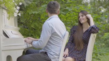 Piyano çalan orta yaşlı adama hayran olan güzel esmer kadının portresi. Kafkasyalı kız arkadaşın müzik dinliyor. Açık havada çıkan yaratıcı romantik çift..
