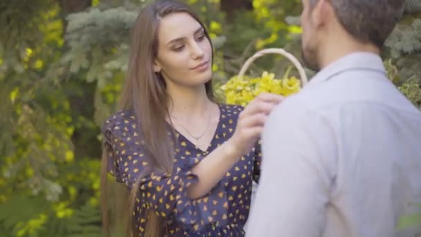 Krásná milující žena upravující košili rozmazaného muže středního věku a usmívající se. Portrét nádherné mladé kavkazské manželky randění s manželem venku v slunečný letní den. — Stock video