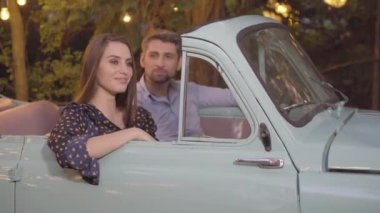 Retro arabada oturan mutlu güzel bir kadın ve arka plandan konuşan bulanık bir adam gibi kameraya gülümsüyor. Açık havada sevgilisiyle çıkan muhteşem beyaz kız arkadaşının portresi..