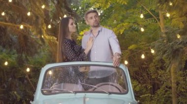 Romantik çift retro arabada dikiliyor ve konuşuyor. Tasasız beyaz erkek ve kadın portresi. Yaz akşamları açık havada çıkıyorlar. Mutlu sevgili sohbeti..