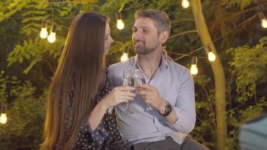 Romantik çift portresi kadeh tokuşturup öpüşüyorlar. Arka planda çelenk ışıkları olan beyaz erkek ve kadınla mutlu bir aşk. Aşk ve aşk kavramı.