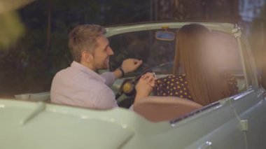 Arka planda, mutlu çiftin eski arabada oturup el ele tutuşup konuşmalarının görüntüsü. Açık havada romantik bir yerde flört eden beyaz erkekleri ve kadınları seviyorum. Mutlu sevgili portresi..