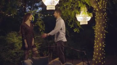 Etrafta romantik ışıklar varken mutlu koca öpüyor ve karısına sarılıyor. Yazın dışarıda buluşan ve gülen beyaz bir çiftin portresi. Sonsuz aşk, romantizm.