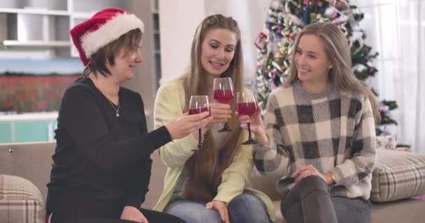 Tre amiche caucasiche allegre che si accarezzano bicchieri di vino rosso e parlano. Ritratto di donne positive che celebrano la vigilia di Natale a casa all'interno. Cinema 4k ProRes HQ. — Video Stock