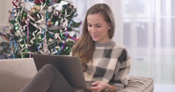 Весела красива жінка дивиться комедійний фільм онлайн на ноутбуці. Портрет молодої кавказької жінки, яка проводить різдвяні канікули на самоті вдома. Новорічна самотність. Фільм 4k ProRes HQ. — стокове відео