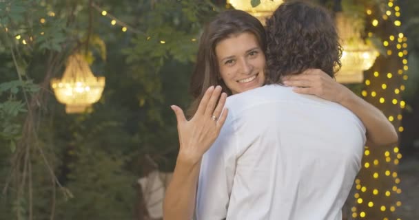 Beautiful brunette Caucasian woman with brown eyes hugging boyfriend and bragging engagement ring on finger. Portrait of happy young bride dating with fiancee on summer evening. Cinema 4k ProRes HQ. — Stock Video