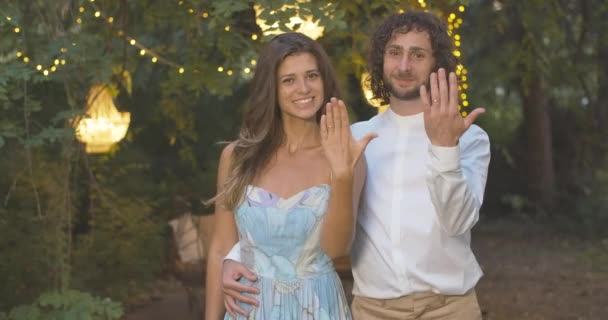 Счастливая невеста и невеста хвастаются обручальными кольцами в летний вечер. Портрет счастливой молодой кавказской пары с драгоценностями на пальцах и улыбкой. Штаб-квартира кинотеатра 4k ProRes. — стоковое видео