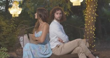 Tartışmalı genç çiftin el ele tutuşup sırt sırta oturuşunun yan görüntüsü. Romantik bir buluşmada beyaz bir kadınla bir erkeğin anlaşmazlık yaşamasını sevmek. İlişki sorunları. Sinema 4k ProRes Merkezi.