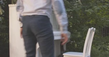 Yaratıcı erkek piyanist piyanoya geliyor bahçede duruyor ve çalmaya başlıyor. Yazın akşam açık havada sanatsal açıdan zarif, beyaz bir müzisyen. Yaşam tarzı konsepti. Sinema 4k ProRes Merkezi.