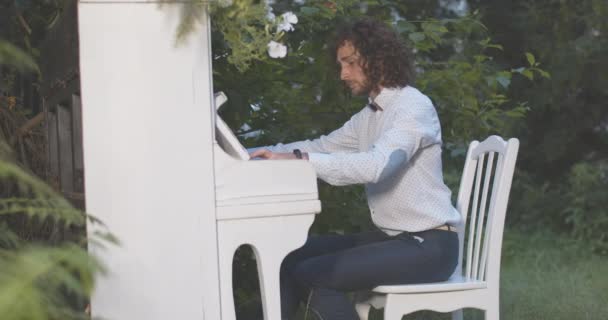 ชายผิวขาวศิลปะจบลงด้วยการเล่นเปียโน ปิดเครื่องดนตรี และเอนหลัง ภาพด้านข้างของนักดนตรีกระตือรือร้นแสดงกลางแจ้งในตอนค่ํา โรงภาพยนตร์ 4k ProRes HQ . — วีดีโอสต็อก