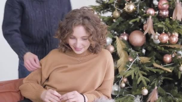 Szerető fiatalember ölelgeti a nőt, és arcon csókolja a társát. Egy boldog fiatal kaukázusi pár portréja, akik együtt töltik a karácsonyt a házban. Romantikus újévi ünnepek. — Stock videók
