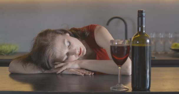 Rack focus verandert van wijn naar dronken brunette vrouw die op de tafel slaapt. Portret van een volwassen blanke vrouw in rode jurk die 's avonds alleen thuis rust. Cinema 4k ProRes Hoofdkwartier. — Stockvideo