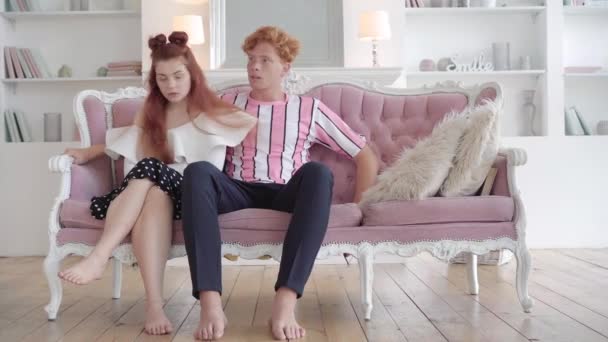 一对有争议的红头发夫妇坐在家里的粉色沙发上的画像。四分卫的白人男男女女在客厅里关系问题和冲突的概念. — 图库视频影像