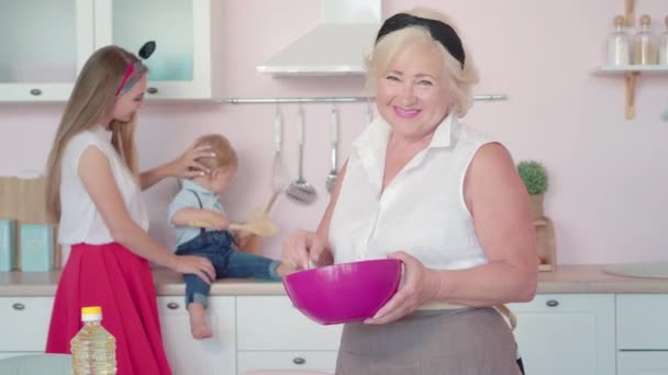 Porträt einer glücklichen Seniorin, die in der Küche Eier schlägt und auf fröhliche Tochter und Enkel zurückblickt. Die pflegende Oma kocht zu Hause das Mittagessen. Glück und Rentenkonzept. — Stockvideo