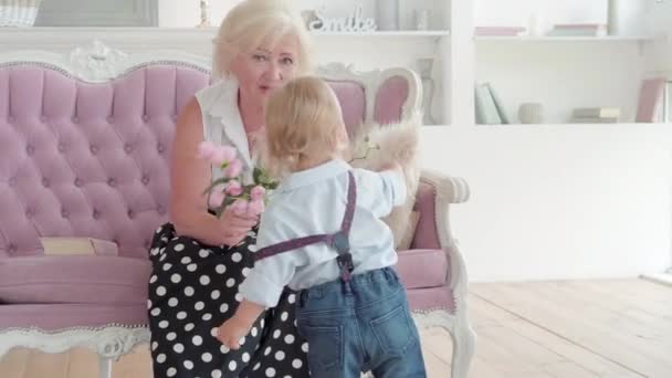 Retrato de la feliz abuela caucásica recibiendo flores de su nieto y hablando. Mujer mayor positiva conociendo a lindo niño en vacaciones. Concepto de celebración familiar. — Vídeos de Stock