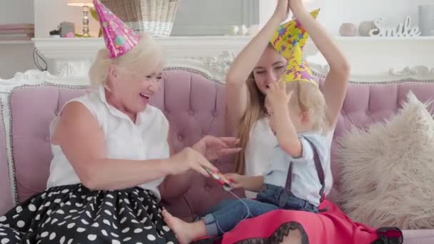 Vrolijke blanke grootmoeder, moeder en zoon vieren vakantie thuis. Portret van een glimlachende familie met feestmutsen die praten en lachen. Eerste verjaardag concept. — Stockvideo