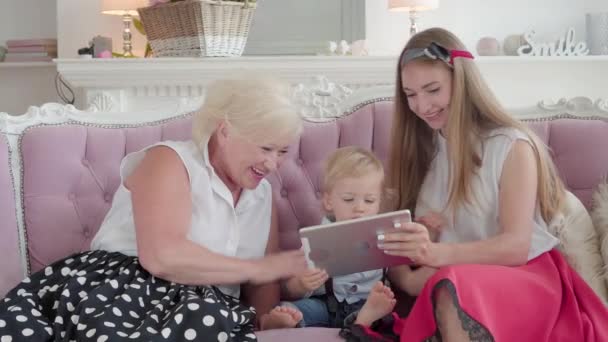 Positiv bedstemor, mor og lille søn taler via videochat på tablet. Smilende kvinder vinker og viser moderne teknologier til søde kaukasiske dreng. Familie fritid koncept. – Stock-video