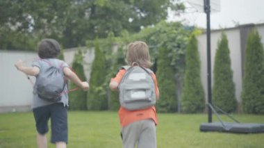 Eve koşan ve sırt çantalarını kusan neşeli öğrencilerin geniş açılı görüntüsü. Neşeli Kafkas kardeşler hafta sonlarını dışarıda kutluyorlar. Çocukluk ve mutluluk kavramı.