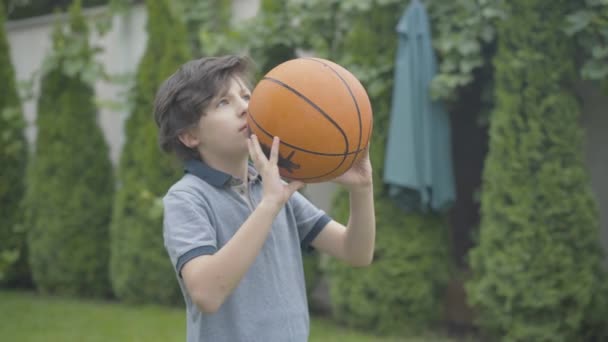 Focado menino morena caucasiano jogando bola e fazendo gesto de vitória. Retrato de criança bonito feliz se alegrando ao ar livre. Criança jogando basquete em casa ou no parque. — Vídeo de Stock