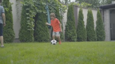 Evdeki yeşil çimlerde futbol oynayan neşeli küçük arkadaşlar ya da kardeşler. Neşeli beyaz çocukların portresi futbol topuna vuruyor ve dışarıda koşuyor. Spor konsepti.